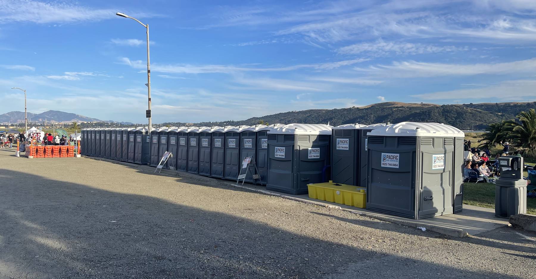 A long row of Pacific Site Services portable restrooms lined up along a Bay Area event field